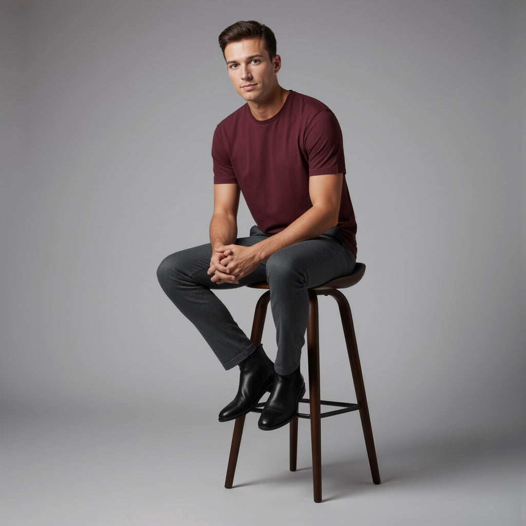 Man sitting on a stool wearing a moleculuxe bordeaux maroon shirt and gray pants against a gray background