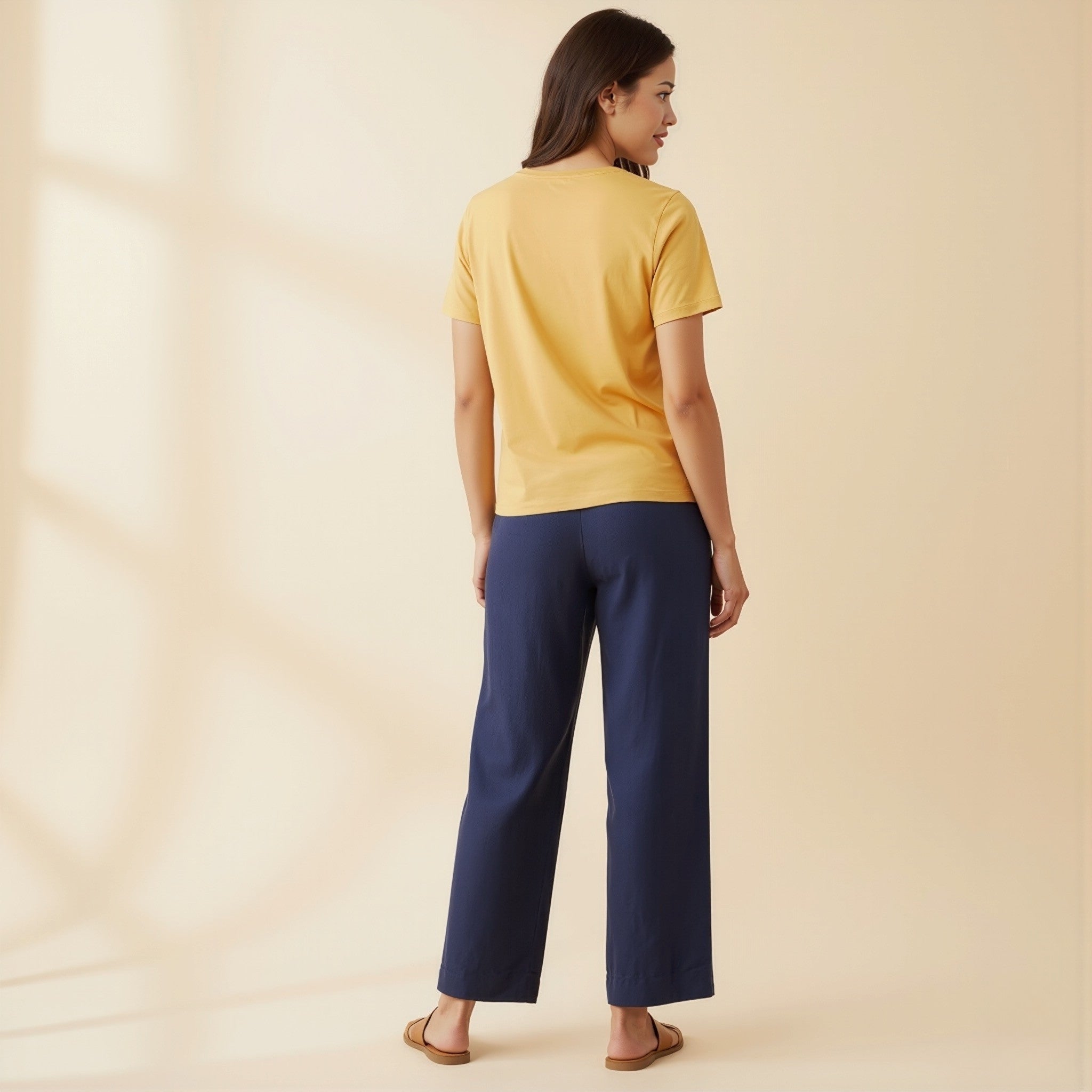 Woman wearing a moleculuxe Champagne Sand yellow top and blue pants on a beige background