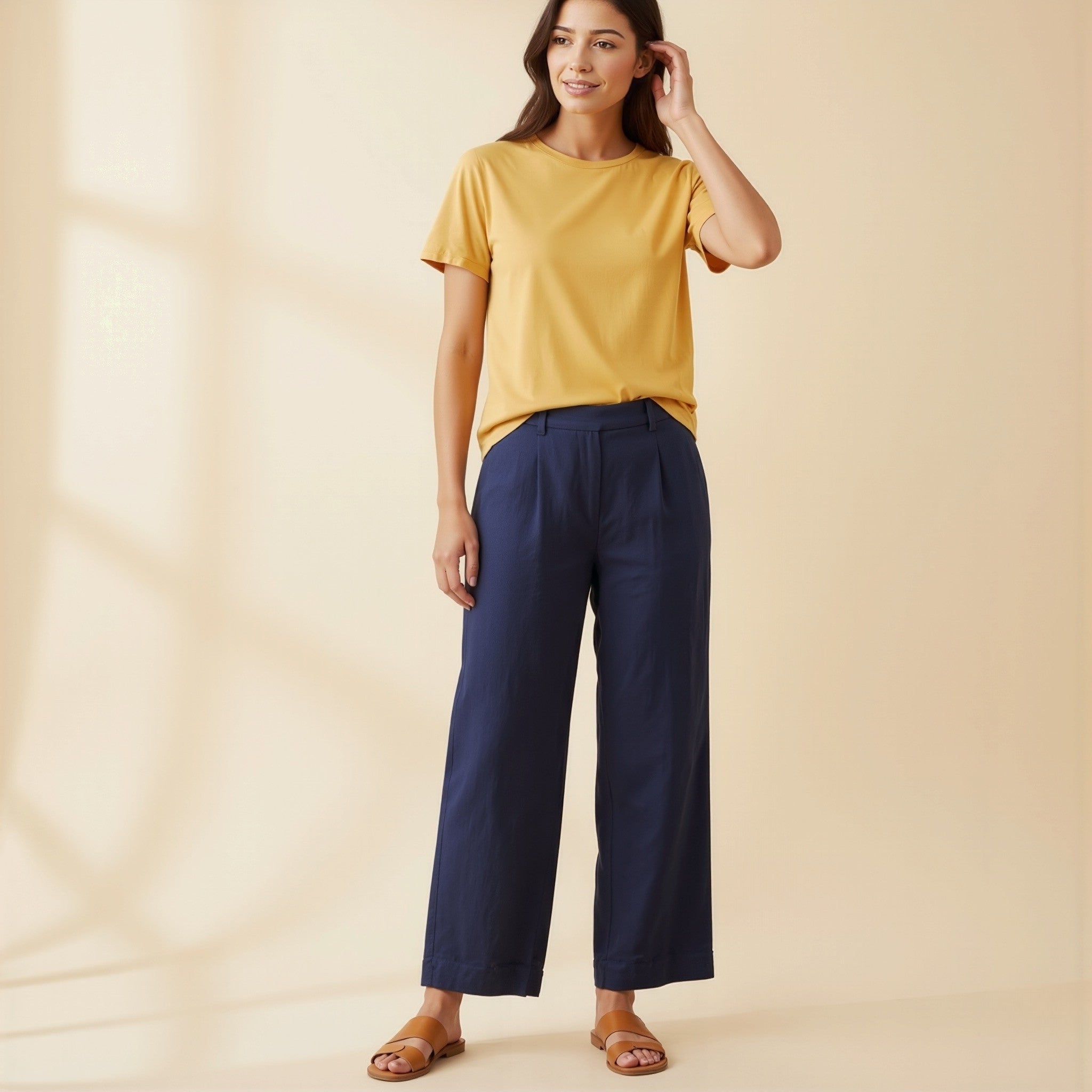 Woman wearing a moleculuxe Champagne Sand yellow top and navy pants on a beige background