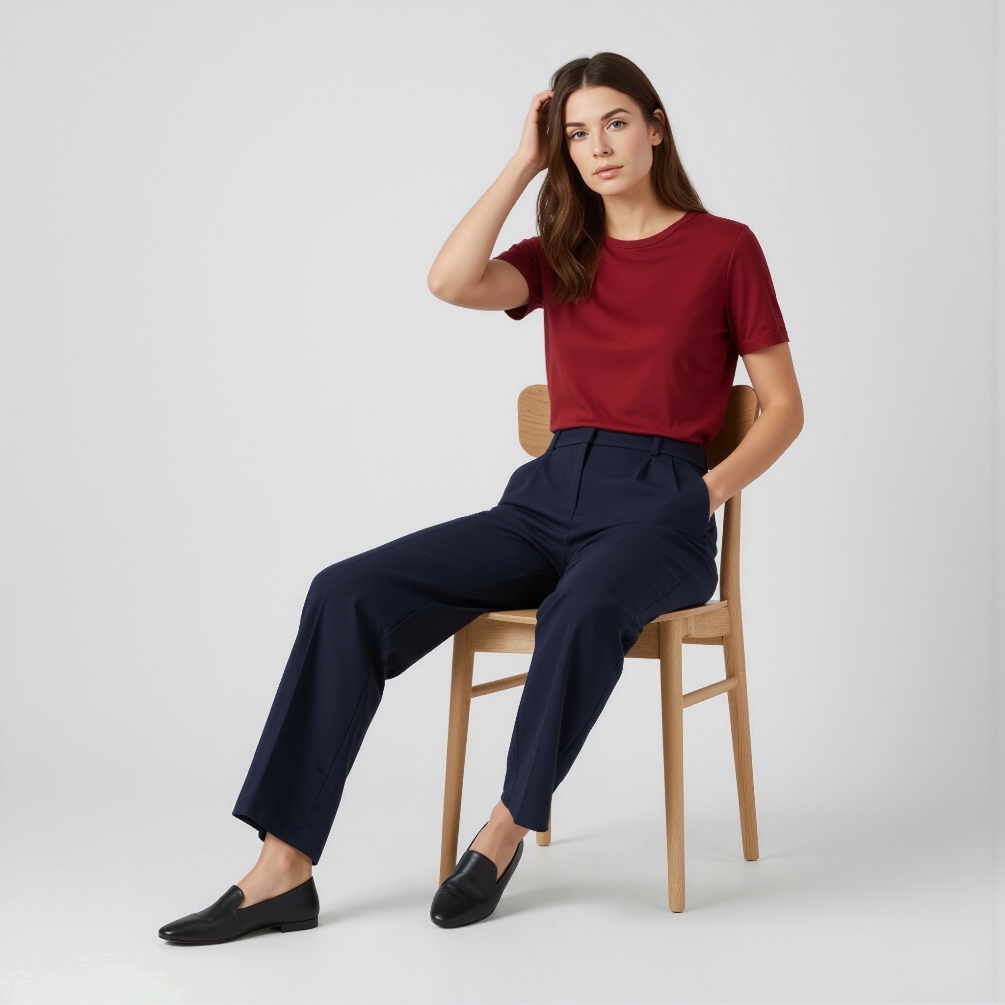 Woman sitting on a chair wearing a moleculuxe Crimson Allure red shirt and navy pants against a white background