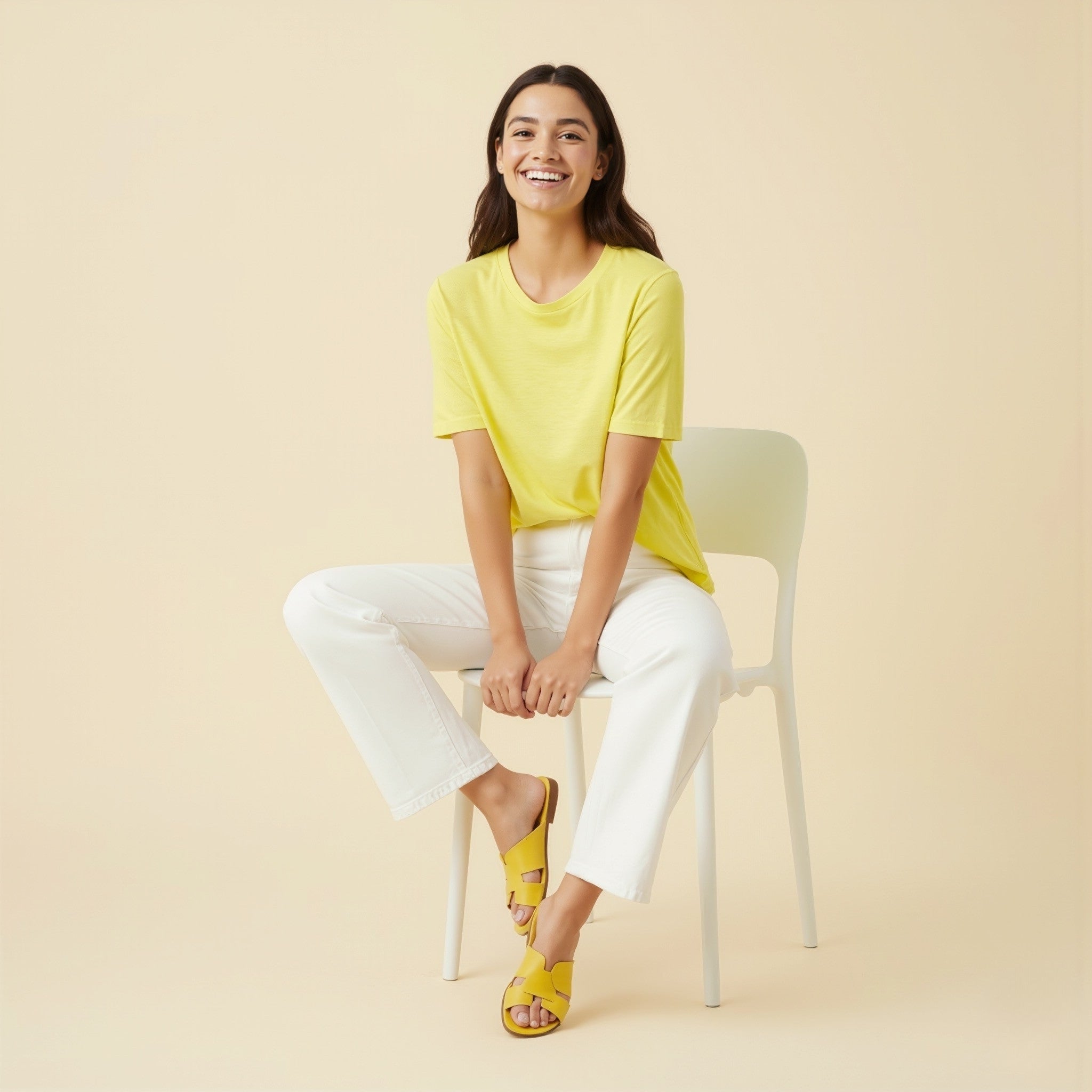 Woman sitting on a chair wearing a moleculuxe lemon zest yellow top and white pants against a beige background