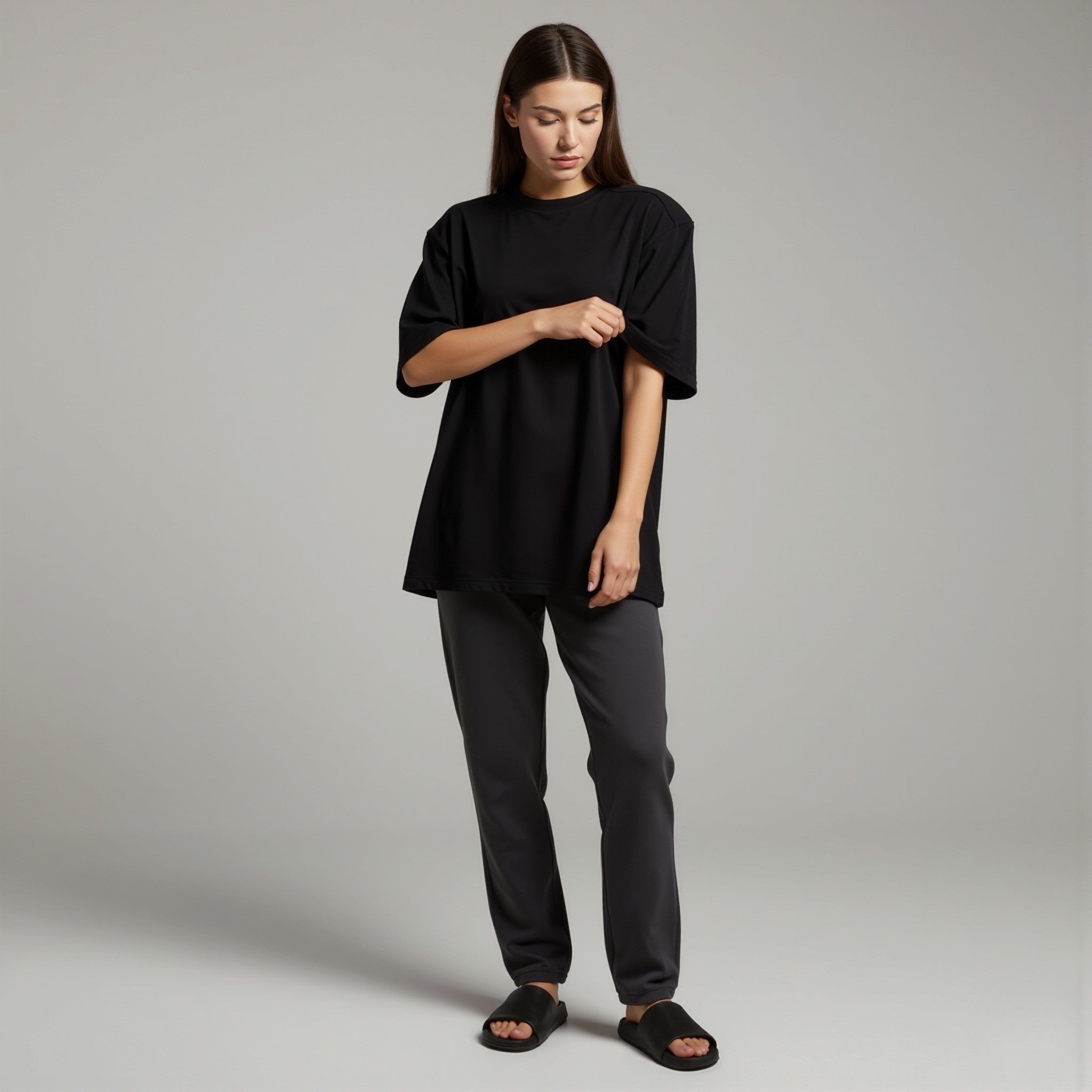 Woman wearing a moleculuxe midnight noir black oversized top and gray pants on a plain background