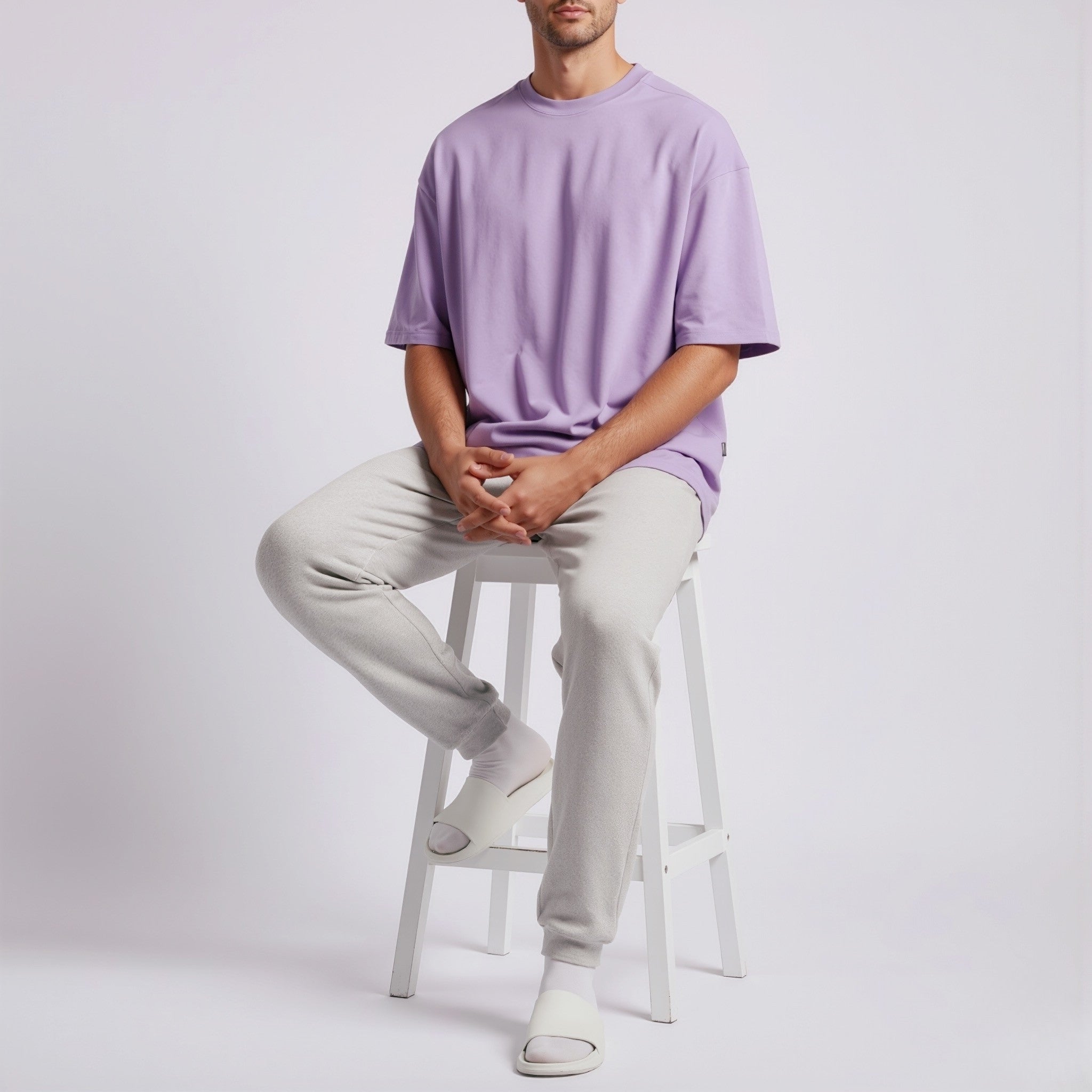 Person wearing a moleculuxe Amethyst Haze purple shirt and light gray pants sitting on a white stool against a plain background