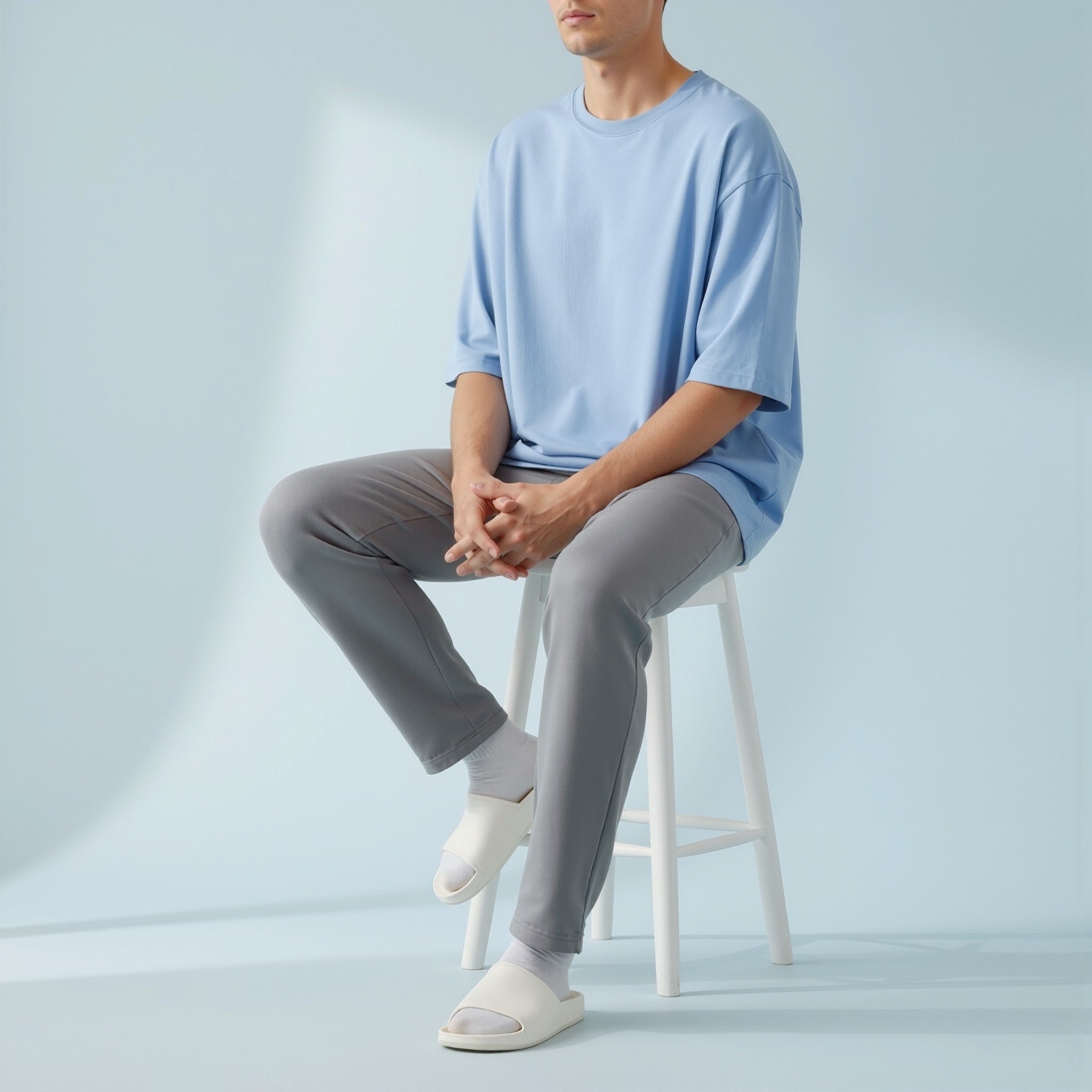 Person wearing a moleculuxe Serene Skies light blue shirt and gray pants sitting on a white stool against a light gray background
