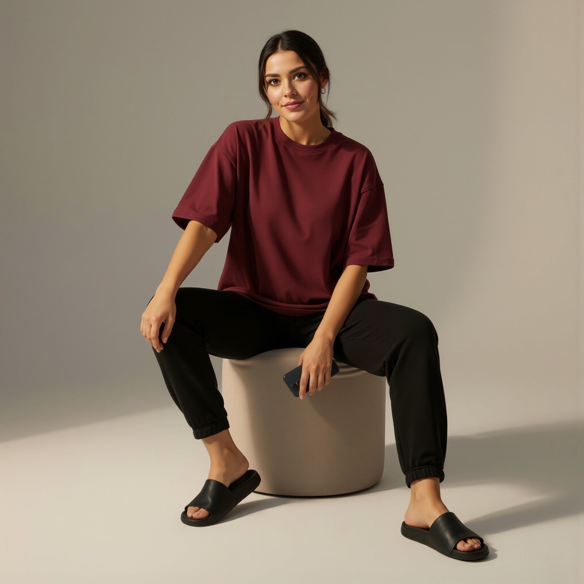 Woman sitting on a gray stool wearing a moleculuxe bordeaux burgundy shirt and black pants against a neutral background