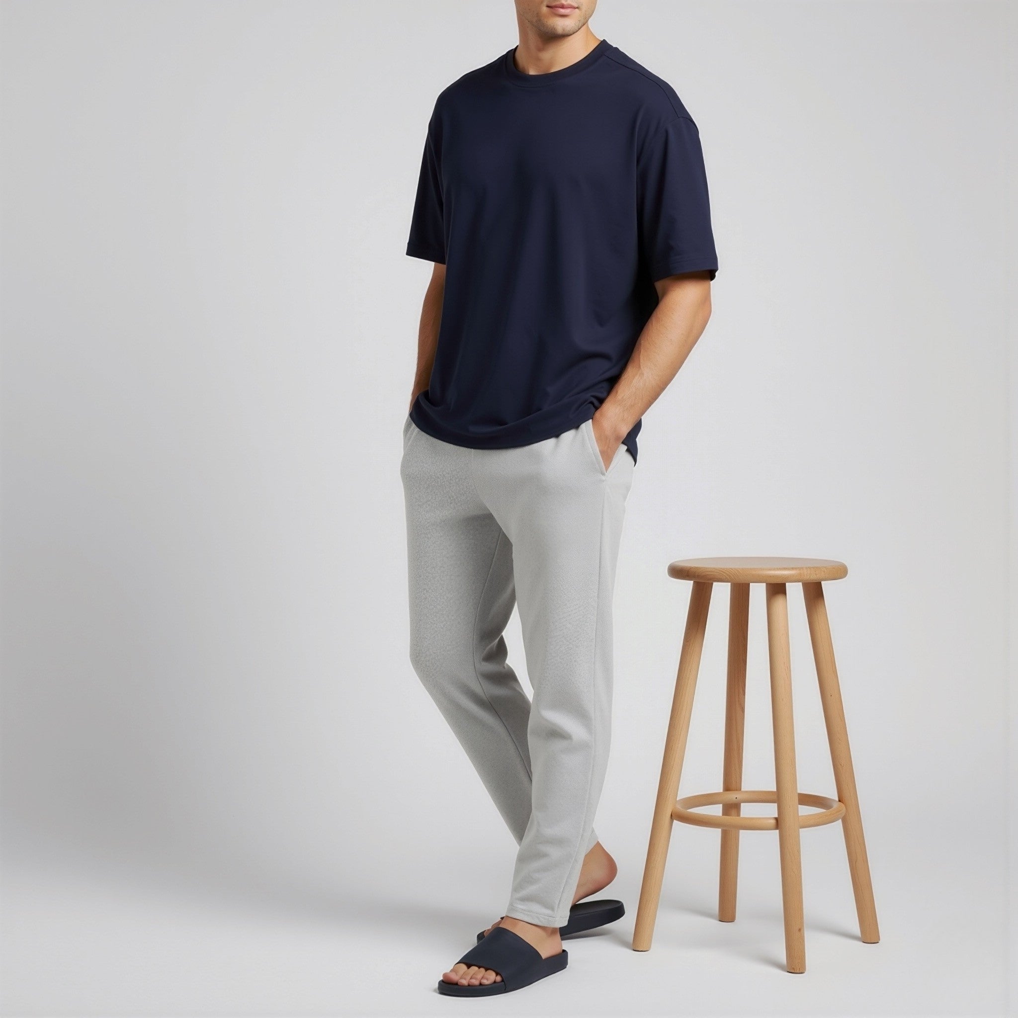 Man wearing a moleculuxe midnight ocean navy t-shirt and light gray pants standing next to a wooden stool on a plain background