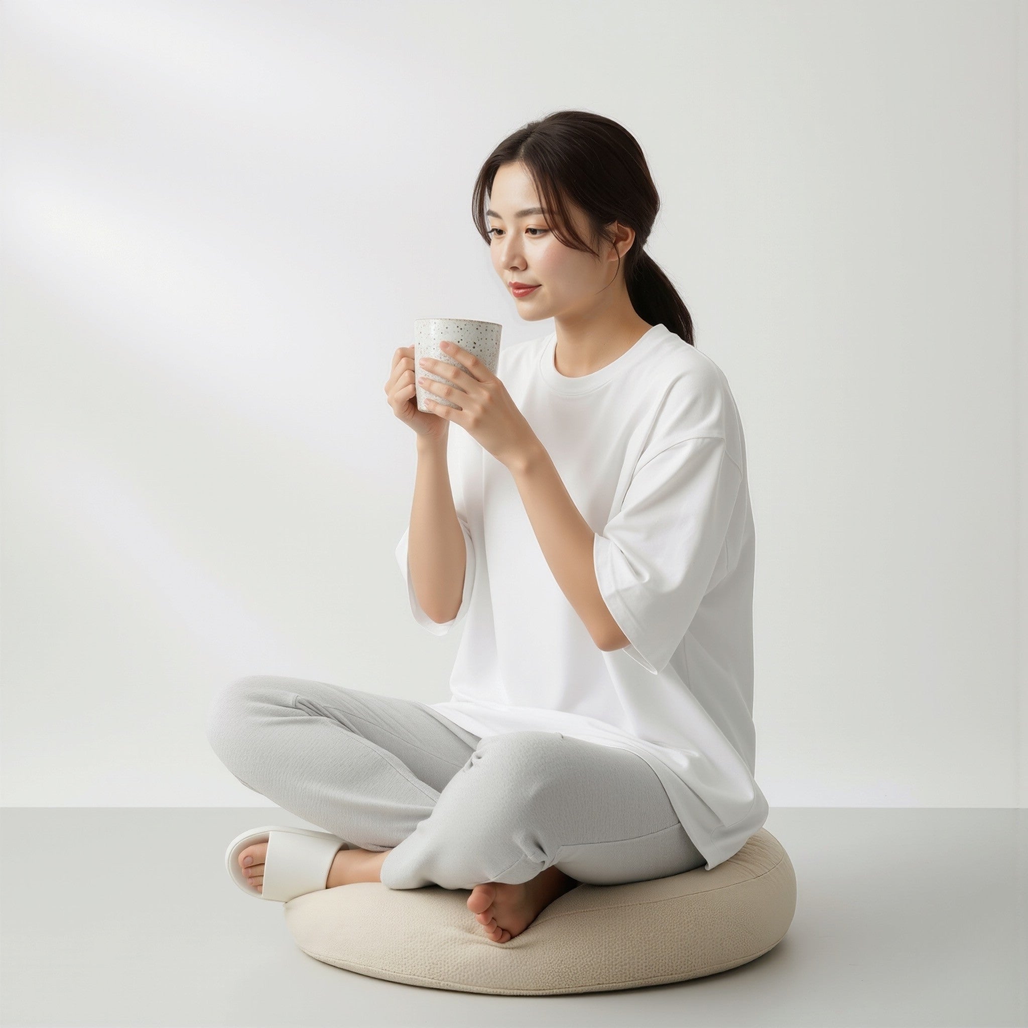 Woman sitting on a cushion wearing a moleculuxe pristine white terry tshirt and holding a mug against a white background