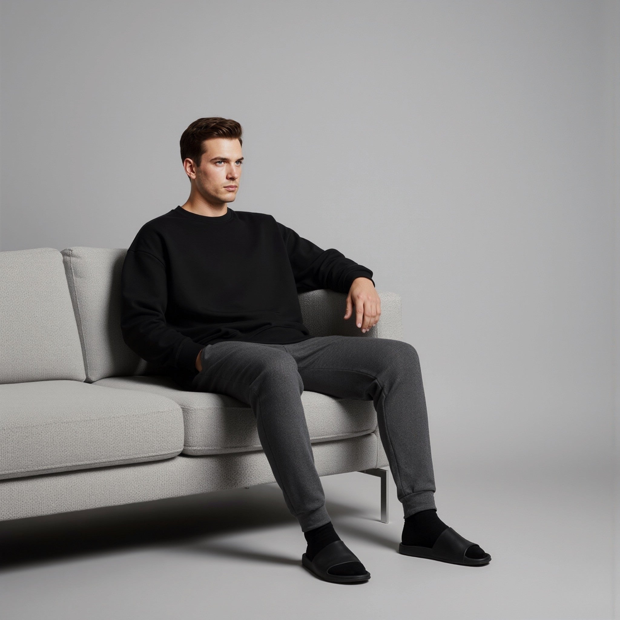 Man sitting on a gray sofa wearing a moleculuxe midnight noir black sweater and gray pants against a plain background