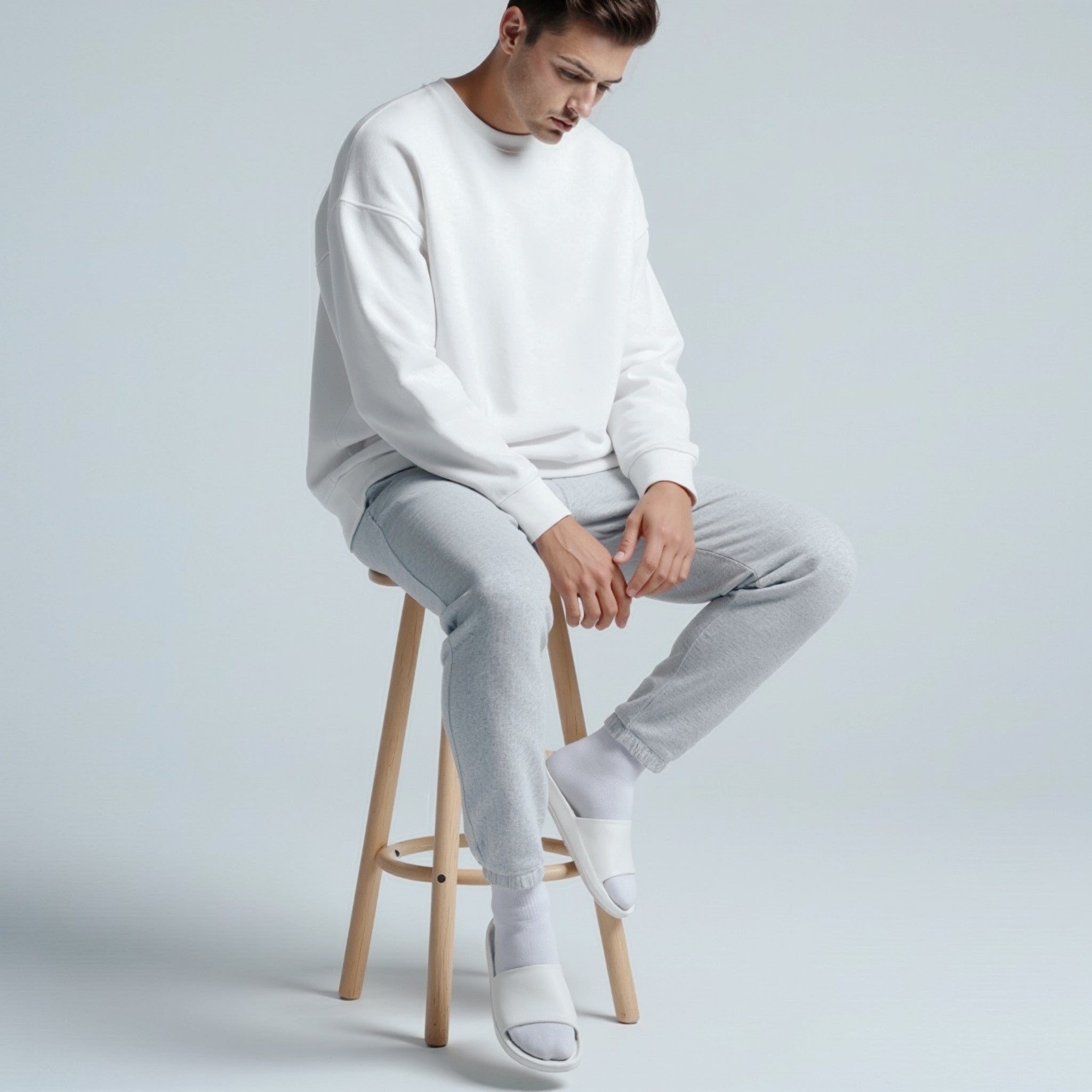 Person wearing a moleculuxe pristine white sweater and light gray pants sitting on a wooden stool against a plain background