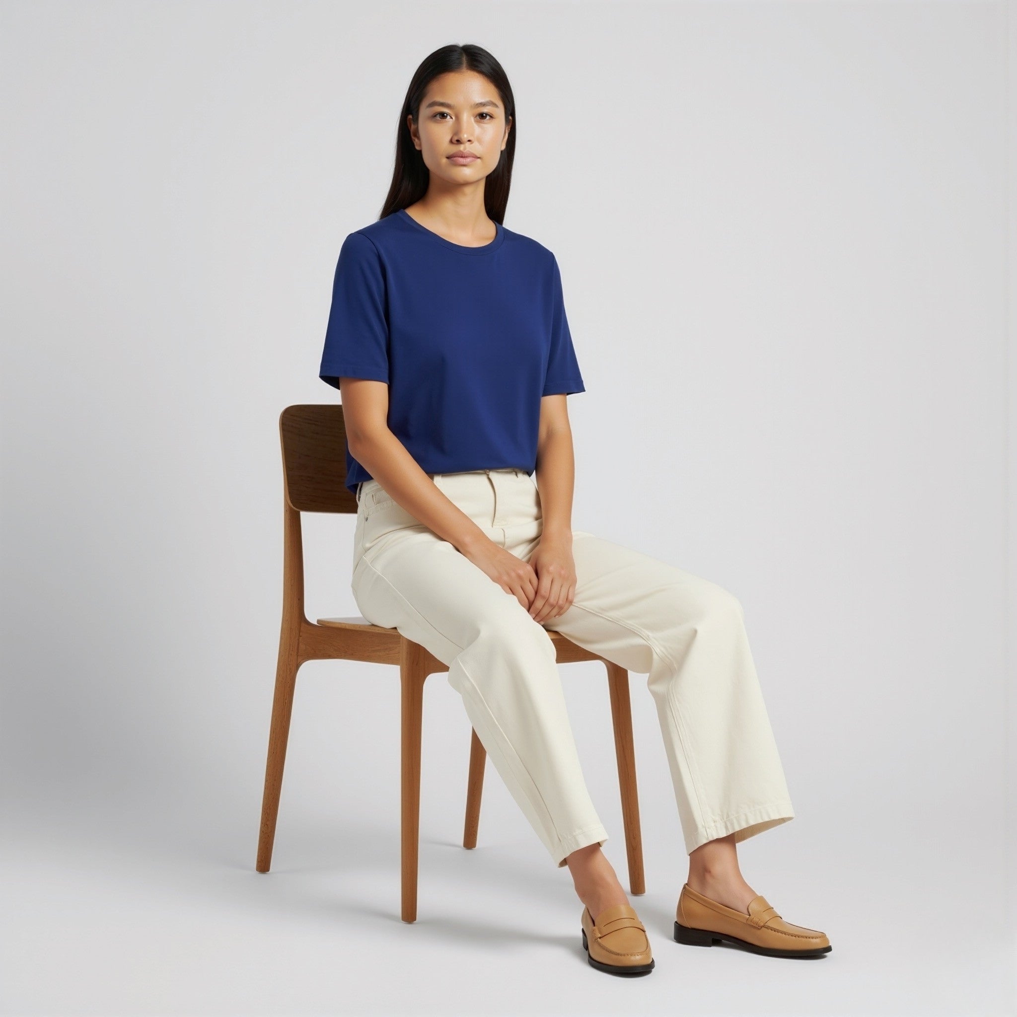 Woman sitting on a chair wearing a moleculuxe Sapphire Majesty blue shirt and white pants against a plain background