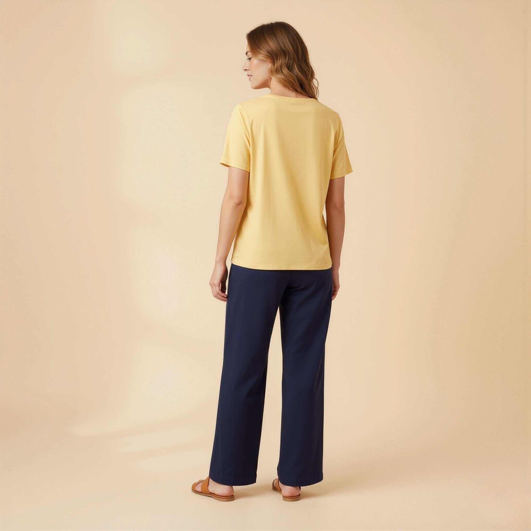 Woman wearing a moleculuxe soft sunflower yellow top and navy pants on a beige background