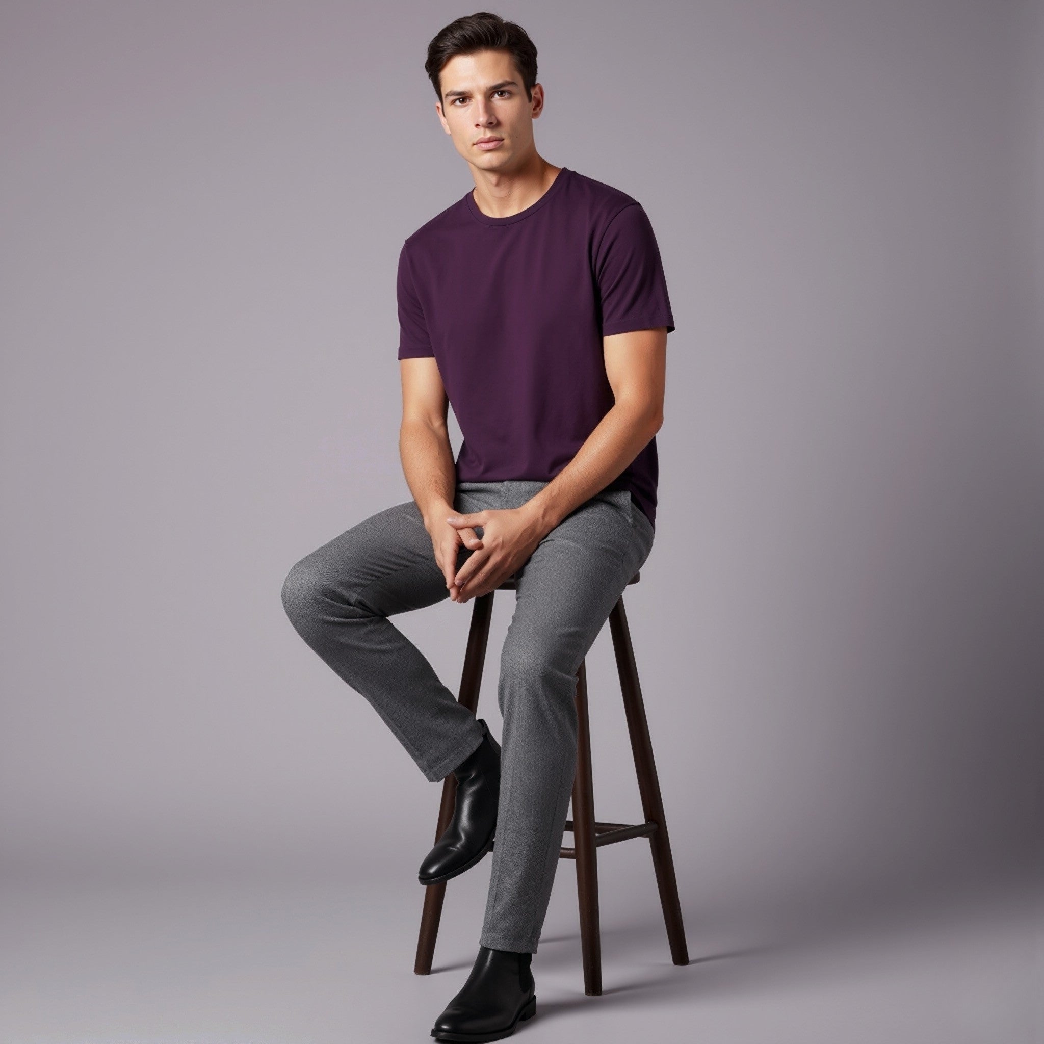 Man sitting on a stool wearing a moleculuxe imperial violet purple shirt and gray pants against a gray background